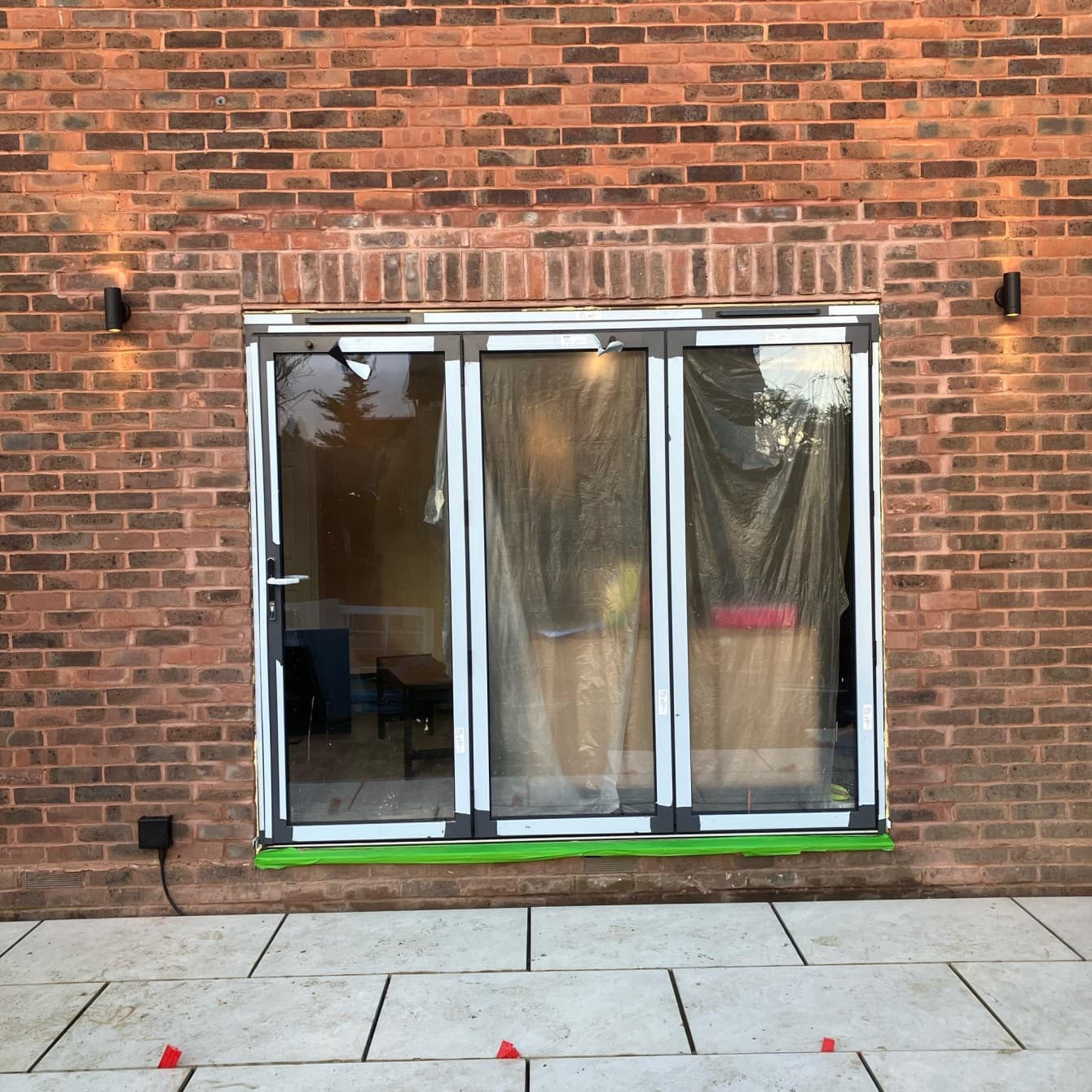 Black up-and-down wall lights fitted either side of bi-fold doors on a brick wall